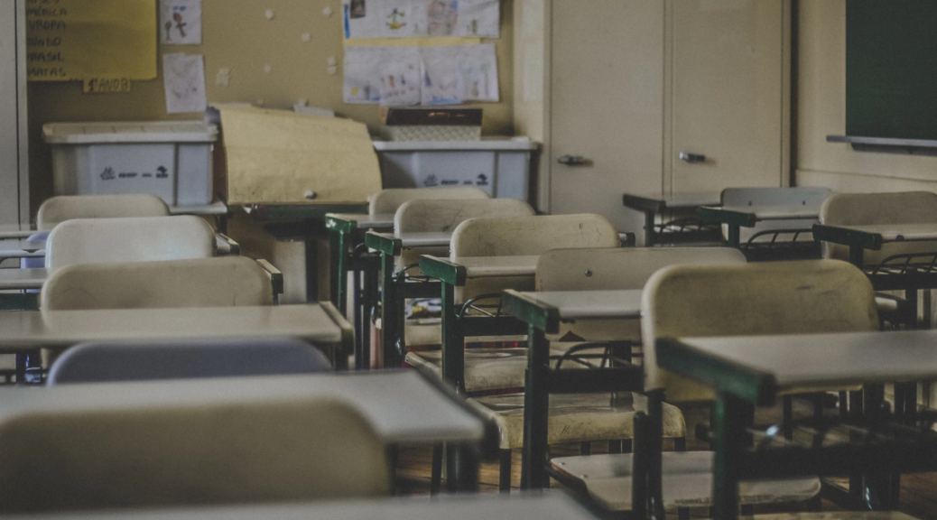 Photograph depicting serried rows of empty desks and chairs in a school classroom.