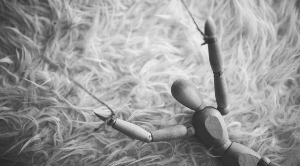 A wooden puppet, controlled by strings, resting on a surface.