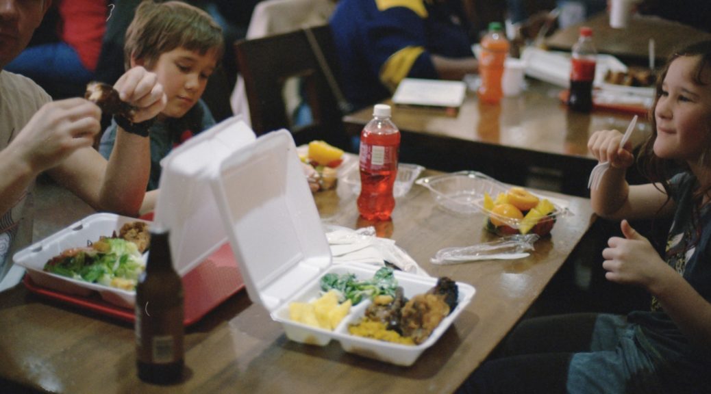 Children sitting at tables eating prepackaged lunches.