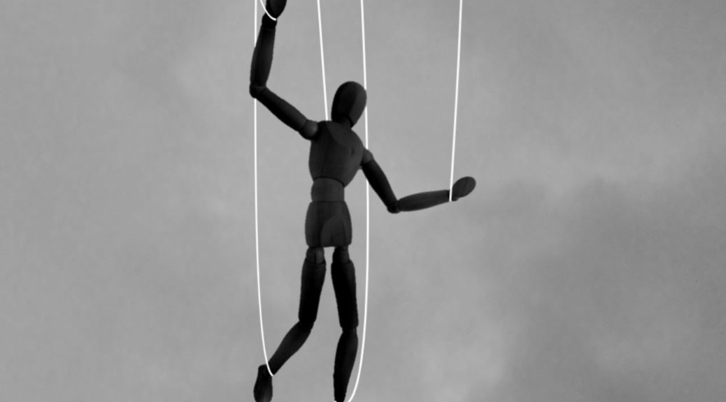 Black and white image of a wooden puppet suspended in the air by four strings.
