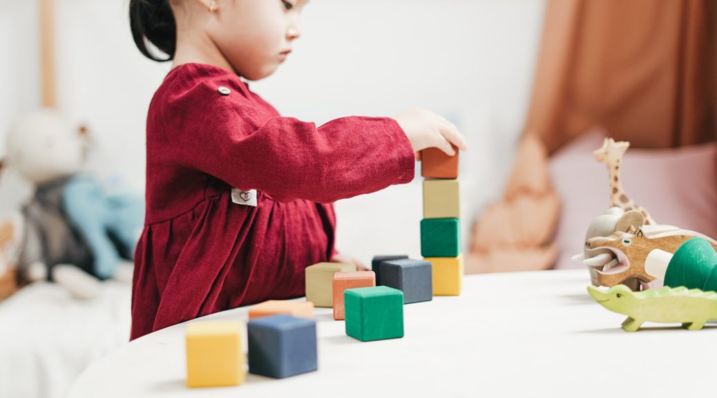 A young girl in a red dress arranging blocks on a table